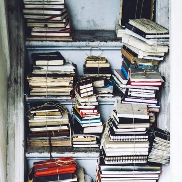 Piles of books on shelves, tied together into bundles. Photo by Simson Petrol on Unsplash